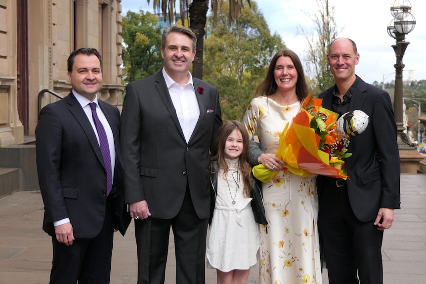 A bride holding flowers stands with her new husband, daughter and two other men.