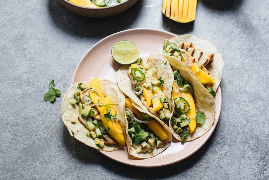 Pink plate with five soft tacos filled with mango ceviche and cucumber avocado salsa.