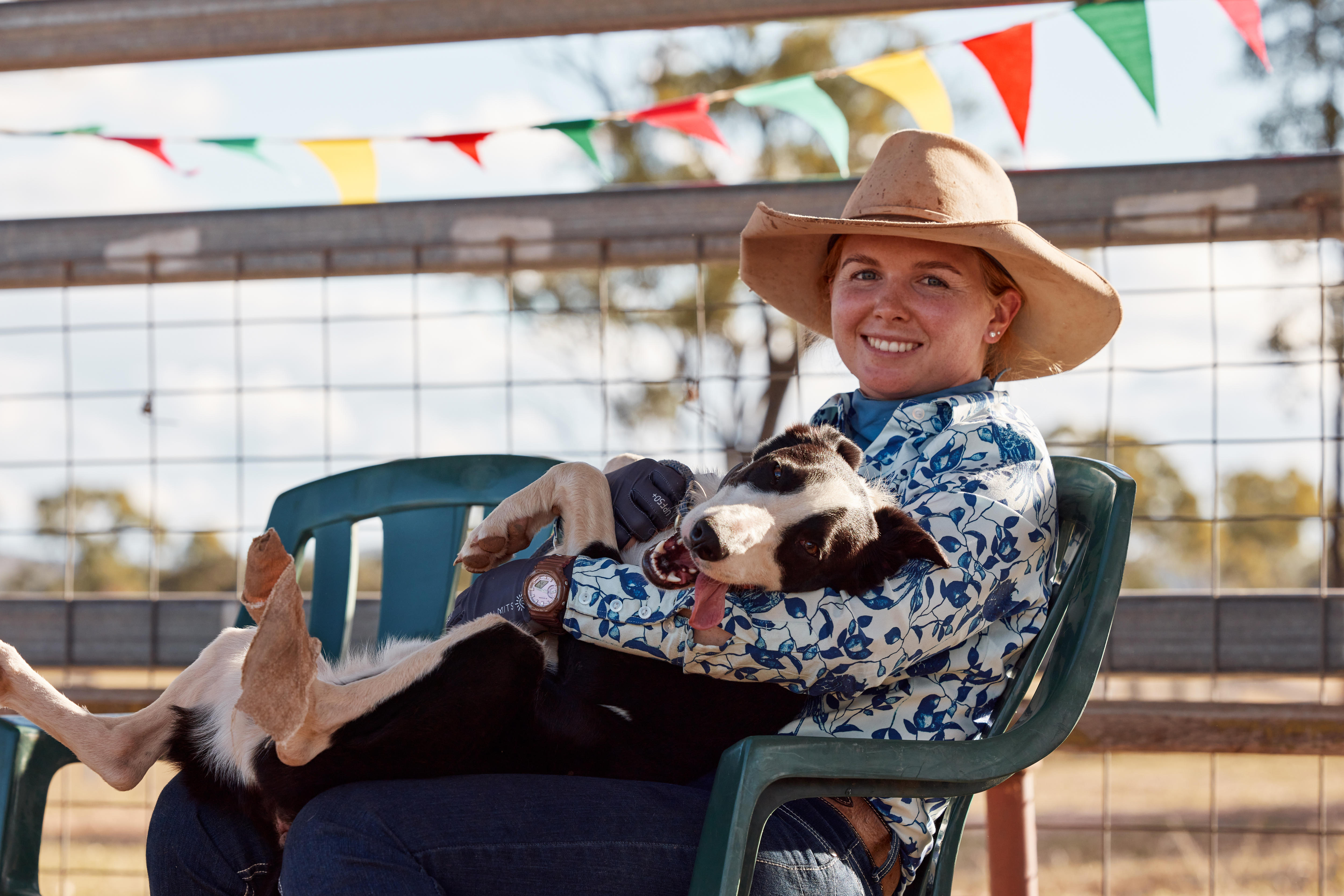 A smiling woman sits in a chair, a dog lazing in her lap.