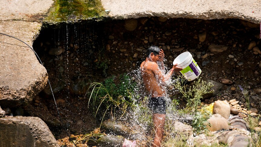 A man cools himself by taking a bath with water collected from a leaking municipal pipe on a hot summer day.