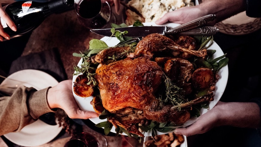 Looking down on a dinner table with roast turkey and wine and people reaching for food