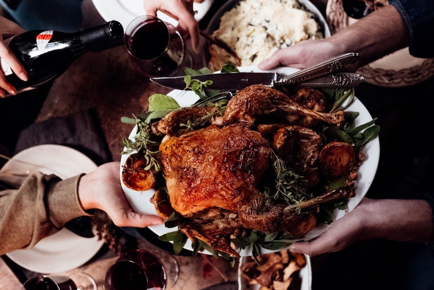 Looking down on a dinner table with roast turkey and wine and people reaching for food