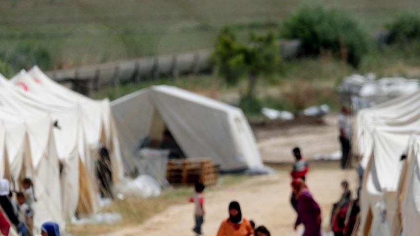 Syrian refugees walk past tents at the Boynuyogun Turkish Red Crescent camp