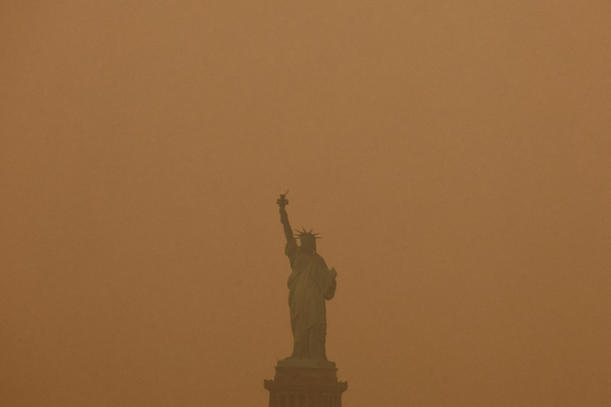 The Statue of Libery surrounded by orange smoke. 