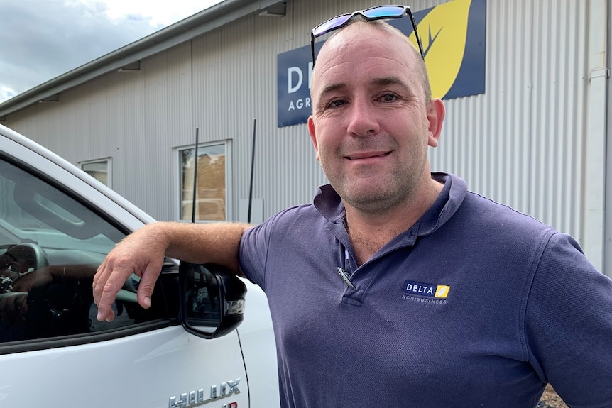 A bald man in a polo shirt leaning on a ute.