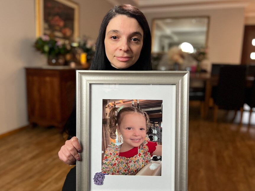 Woman holding framed photograph of a young girl. 