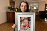 Woman holding framed photograph of a young girl. 