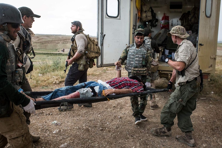 Men in army camouflage load a man on a stretcher into the back of an armoured vehicle.