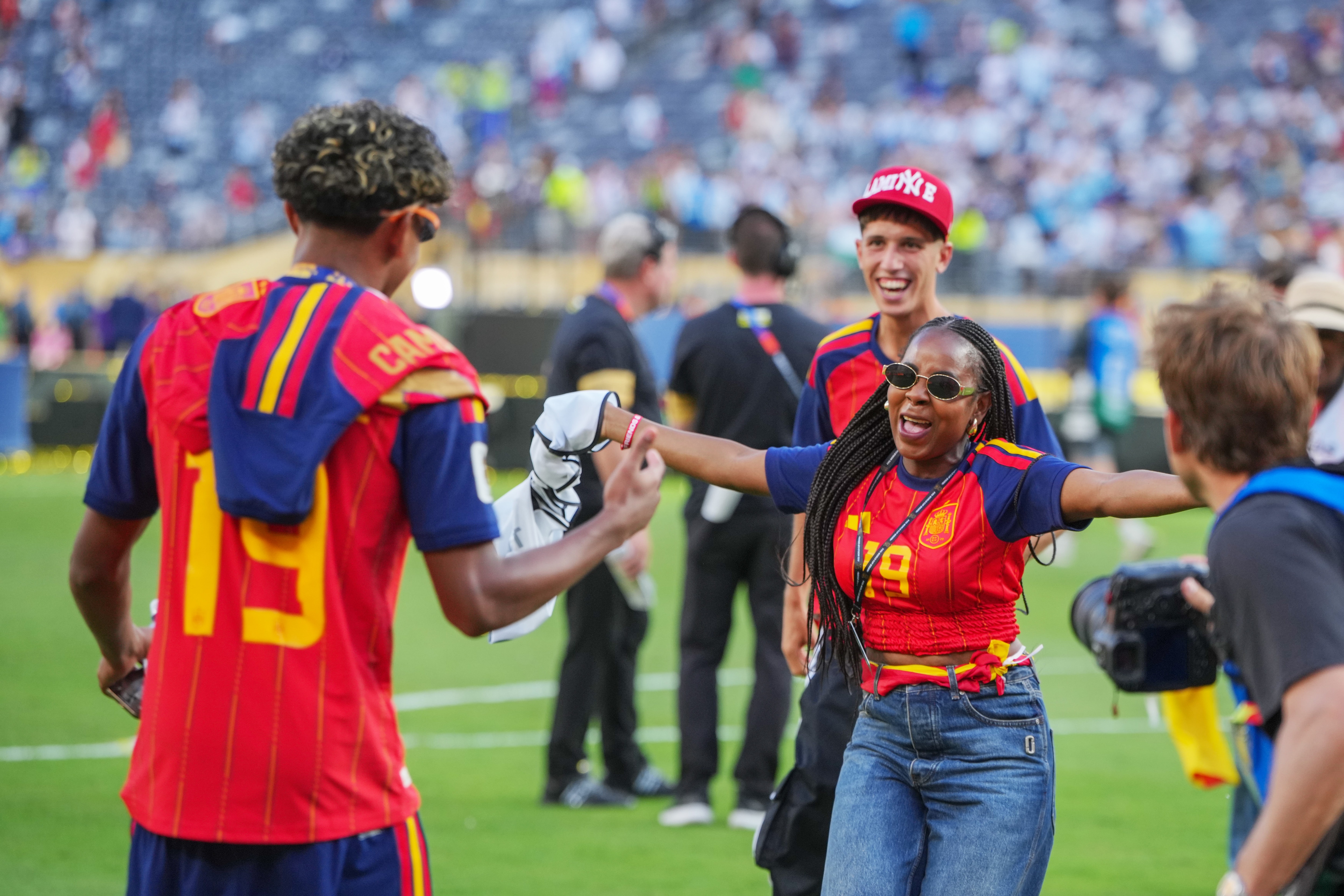 A woman in a red team shirt spreads her arms to embrace a man wearing the same colours.
