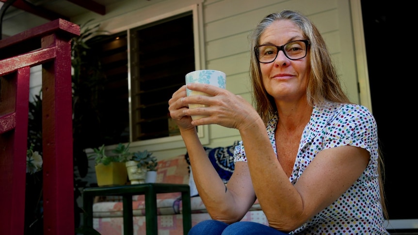 A woman sitting on the steps outside a house, holding a cup of tea.