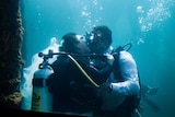 Mand and woman kissing underwater in full scuba gear.