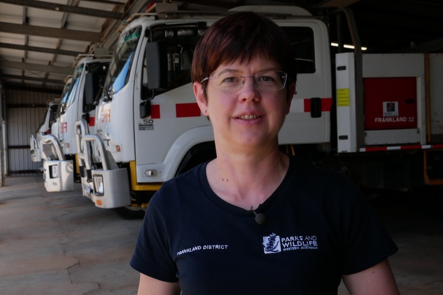 A female WA Parks and Wildlife worker in a garage, standing in front of a line of trucks.