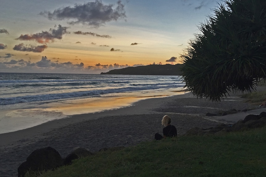 Woman sits looking at Byron Bay's Main Beach at sunrise