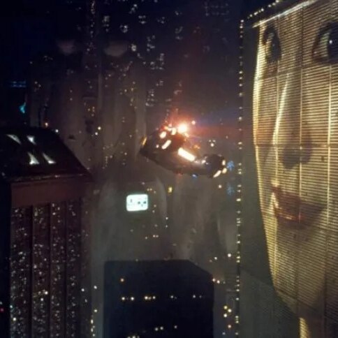 The neon cityscape of the movie Blade Runner - a flying car is floating past a massive video billboard with a woman's face on it