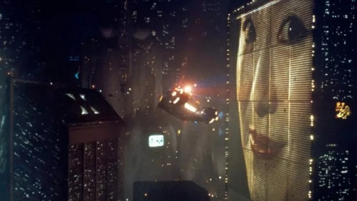 The neon cityscape of the movie Blade Runner - a flying car is floating past a massive video billboard with a woman's face on it