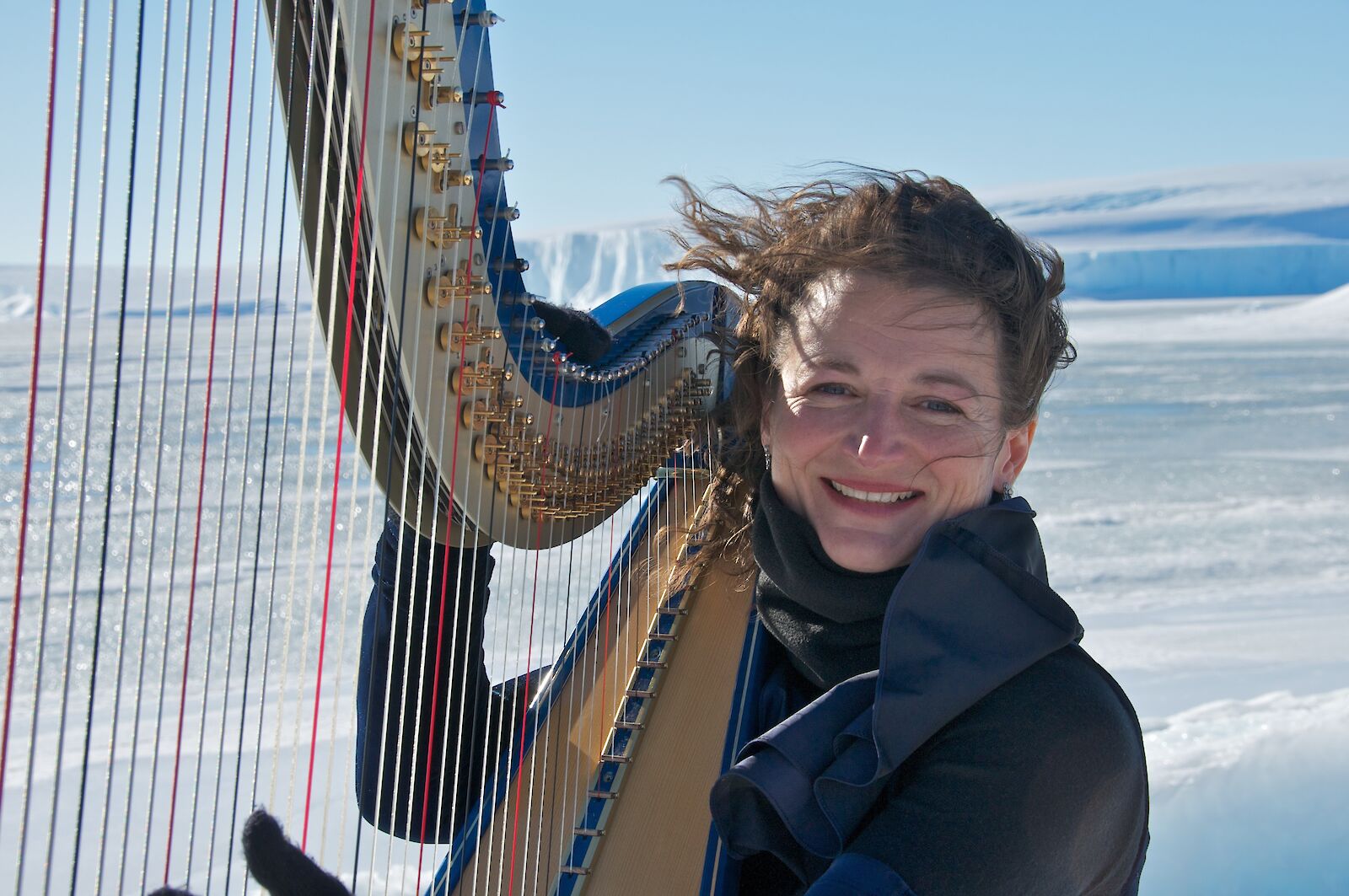 Alice Giles sentada com sua harpa no gelo da Antártida.