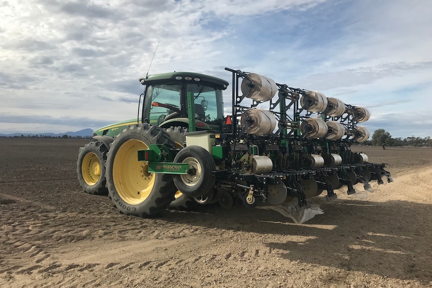 Machinery parked in a field with a modification on the back of it that has rolls of film