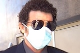 A man walking wearing sunglasses and a face mask.