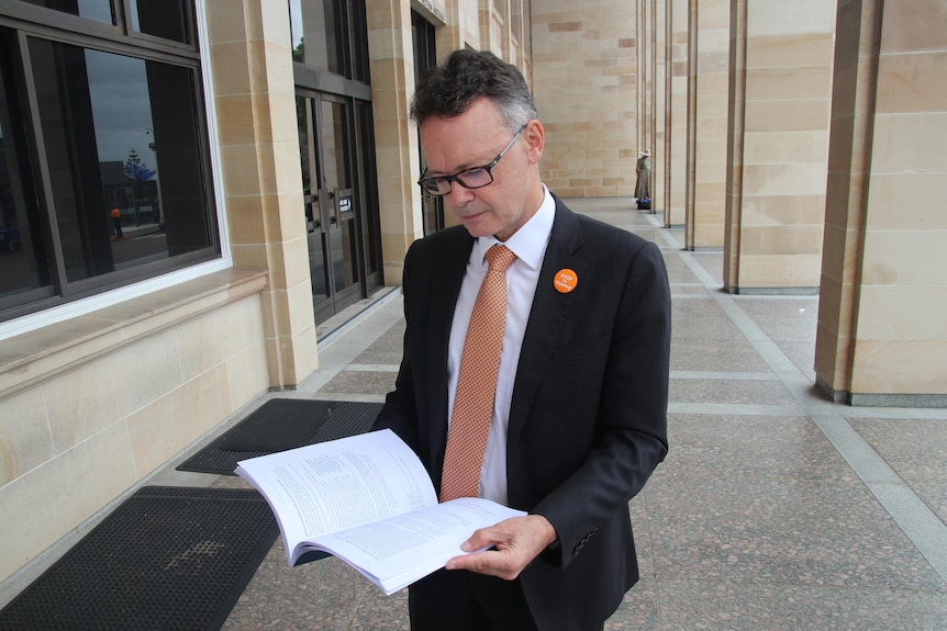 A picture of Chris Tallentire reading the report outside the doors of WA Parliament House