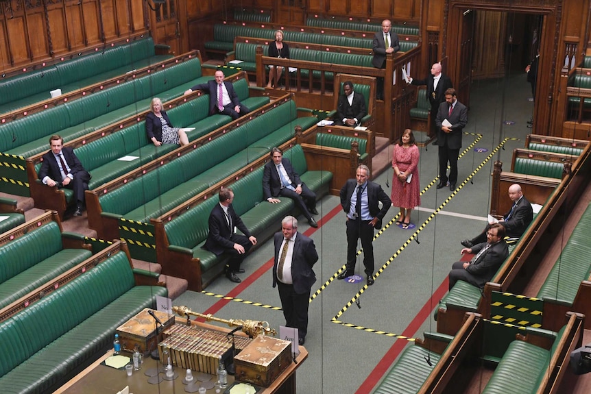 Politicians stand and sit metres apart from each other in the House of Commons. Caution tape and stickers are on the floor