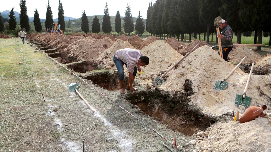 People work on newly dug graves at a cemetery in preparation for the funerals of the miners.