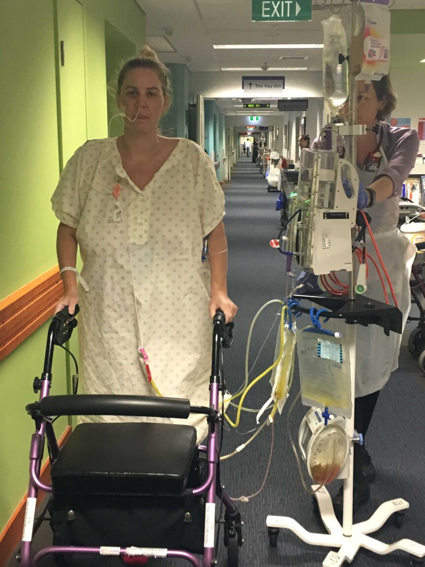 Sally Woods walks down the corridor of a hospital holding on to a walker.
