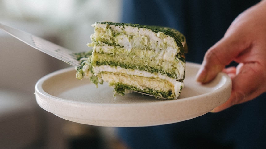 A slice of matcha tiramisu being served onto a white plate using a spatula. The layers of biscuit, cream and matcha visible.