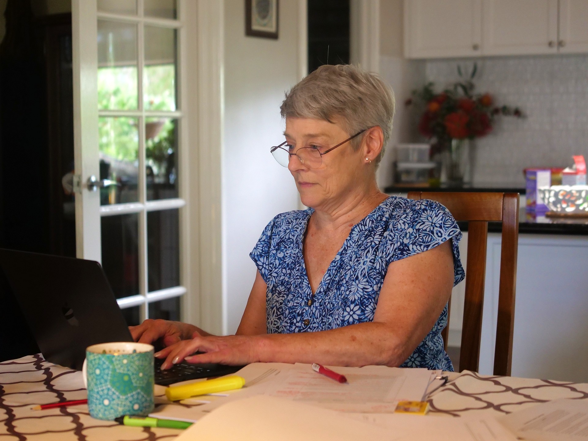 Una mujer sentada frente a una computadora en su cocina.