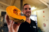 a man stands in a kitchen holding up a kent pumpkin