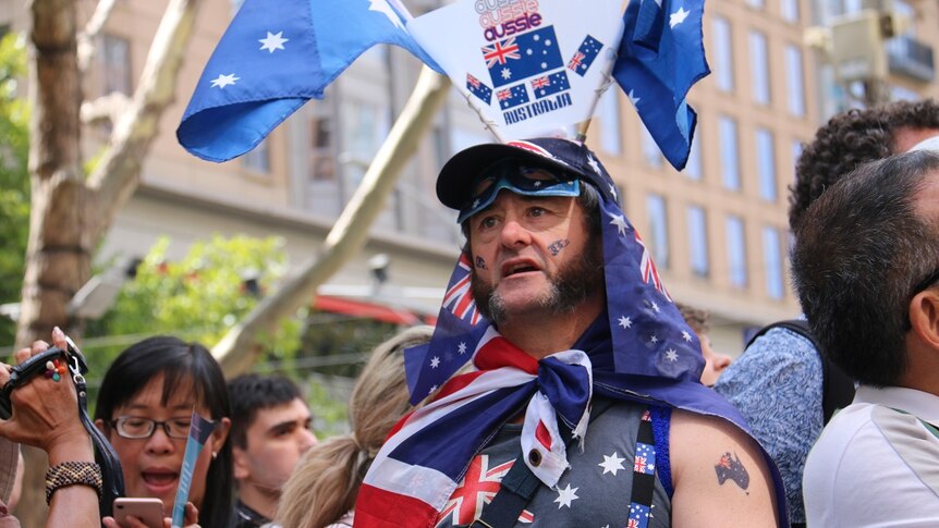 A man decked out with Australian flags, colours and motifs celebrates among a large crowd.