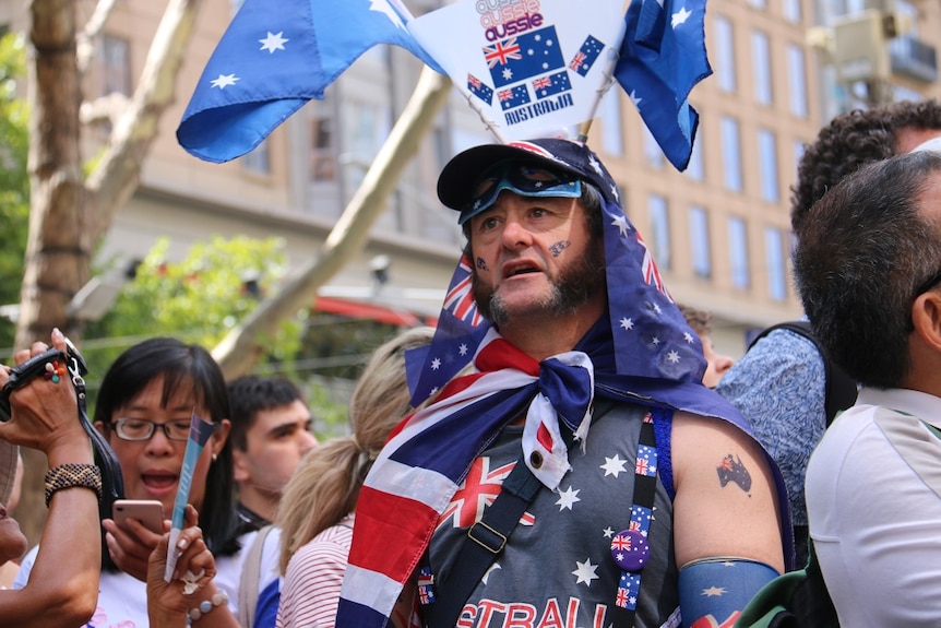 A man decked out with Australian flags, colours and motifs celebrates among a large crowd.