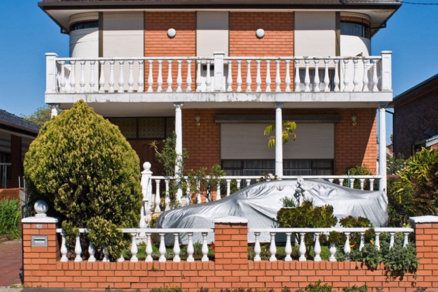 On a bright blue day, you view a orange brick house lined with Italianate balustrades and white Corinthian columns.