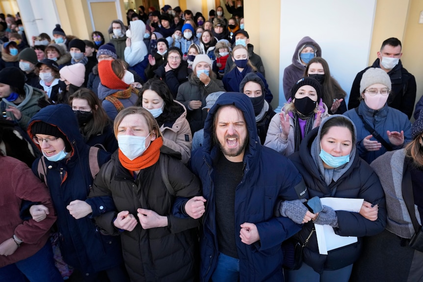 Demonstrators stand with arms linked as they chant slogans during a protest outside a building. 