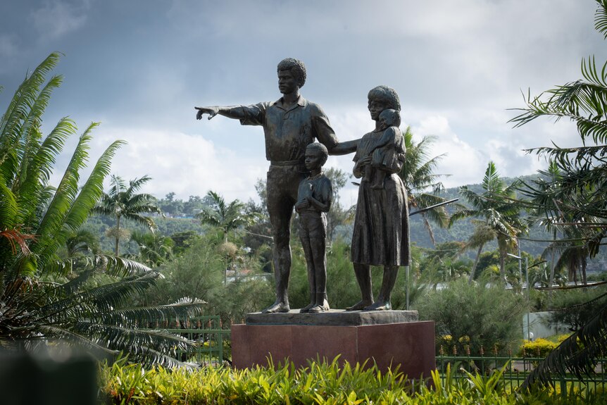 A statute of a family in Vanuatu in the jungle pointing to the left.