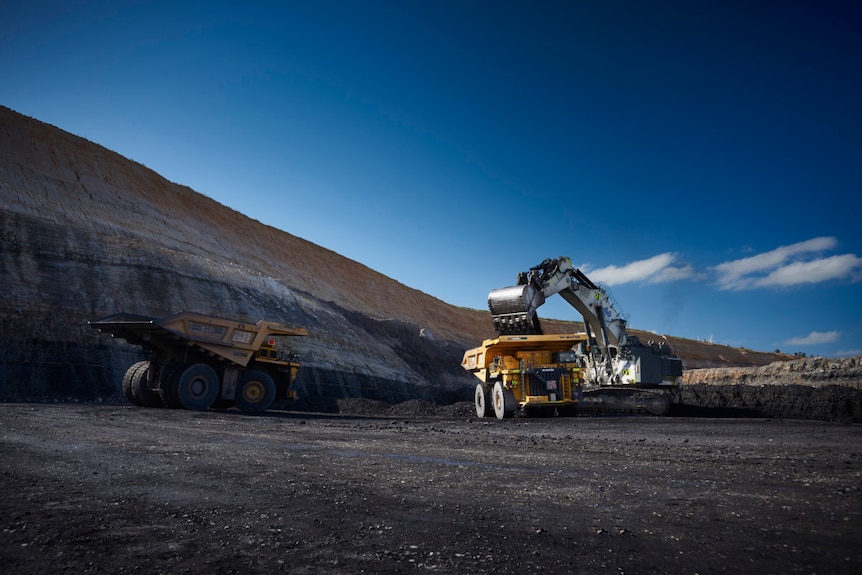 Two mining trucks being filled with coal by a digger