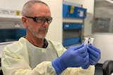 A man wearing a lab coat and goggles holding two test tubes