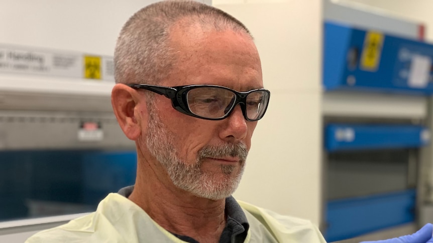 A man wearing a lab coat and goggles holding two test tubes