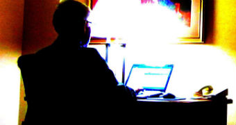 A man sits at a laptop computer in a dark room.
