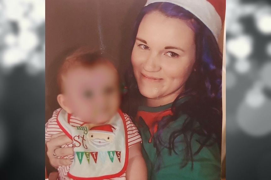Ashley holds a baby and is wearing a Santa hat. The baby's face is blurred.