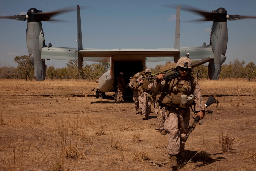 soldiers walk away from a large plane carrying guns and bags