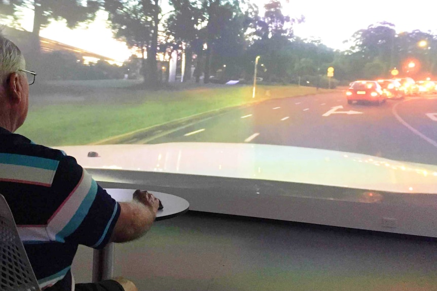 Older man sits at table in front of a big screen showing traffic at dusk