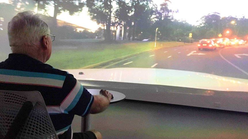 Older man sits at table in front of a big screen showing traffic at dusk