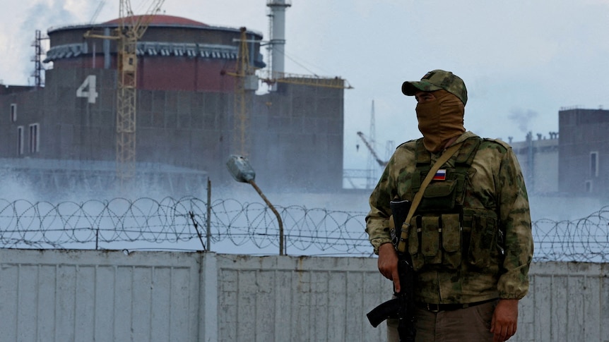 A serviceman with a Russian flag on his uniform stands guard near the Zaporizhzhia Nuclear Power Plant wearing a face covering