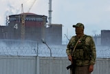 A serviceman with a Russian flag on his uniform stands guard near the Zaporizhzhia Nuclear Power Plant wearing a face covering