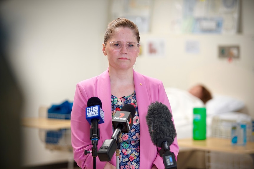 A woman wearing a pink jacket speaking to microphones