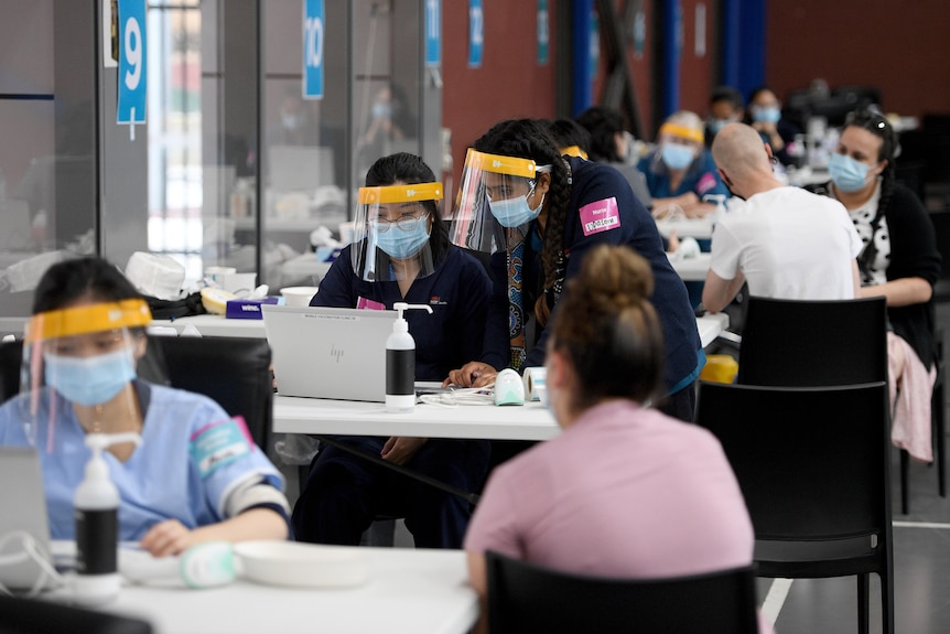 people in a room getting vaccinated by nurses wearing full PPE