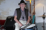 Hubert Davies wears a black hat while sitting at his drum kit.