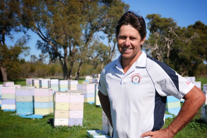 Man in white t-shirt standing in front of bee hives
