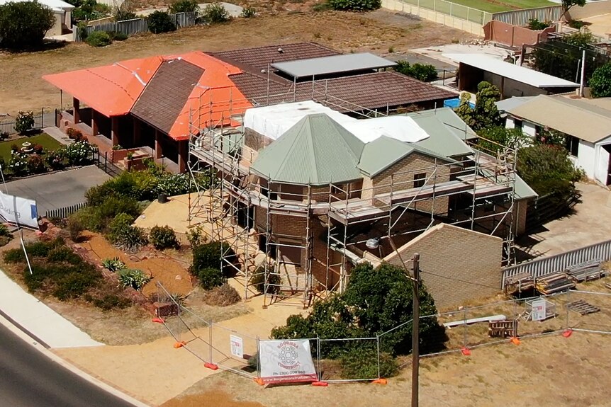 A two storey home with scaffolding and a white tarp on the roof. Behind is a bungalow with an orange tarp.