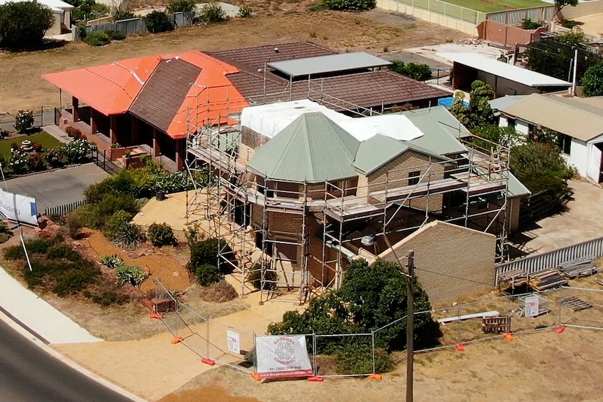 A two-storey home with scaffolding and a white tarp on the roof. Behind is a bungalow, also with a temporary roof covering.